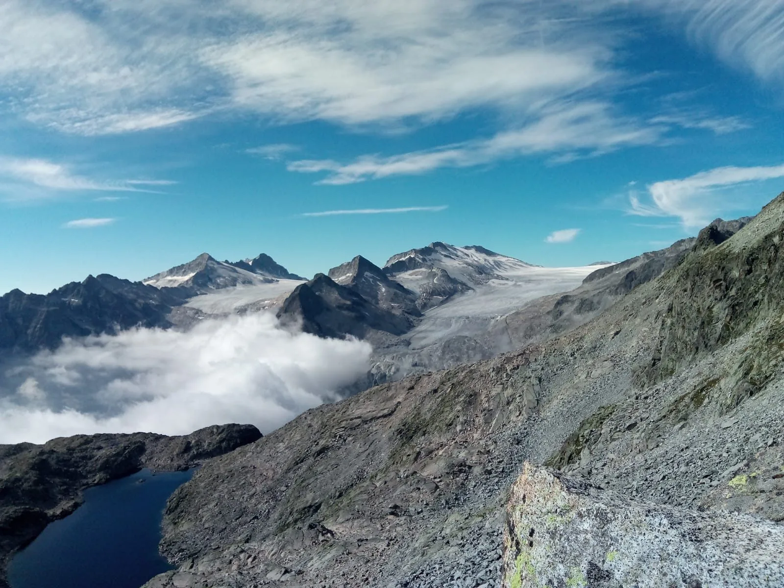 Il ghiacciaio dell'Adamello visto dal Passo Presena, con un lago alpino in basso e nuvole in valle