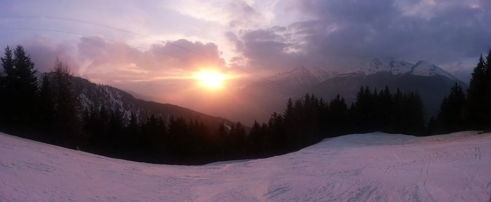La pista del Corno d'Aola innevata al tramonto, tra abeti e cime imbiancate